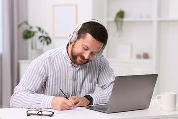 Wall Mural - Interpreter in headphones taking notes while having video chat via laptop at white table indoors