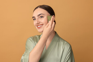 Wall Mural - Beautiful young woman doing facial massage with gua sha tool on beige background