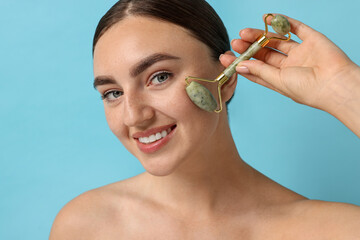 Canvas Print - Beautiful young woman doing facial massage with roller on light blue background