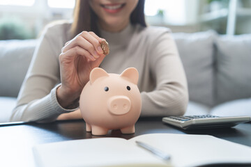 Saving money wealth concept, asian young business woman hand putting coin into piggy for saving cost, cash finance planning to spend enough money on her income for save money, payment tax, investing.