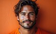 © Gelpi - Handsome man with tousled hair and a beard smiling confidently against an orange background, wearing an orange shirt Generative AI
