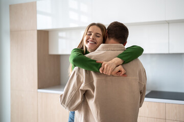 Happy couple standing at home with sincerely embrace, rejoicing in success, fulfillment of dreams and common goal. Overjoyed loving woman smiling hugging husband celebrating new phase of together life