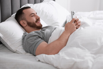 Poster - Smiling man using mobile phone in bed