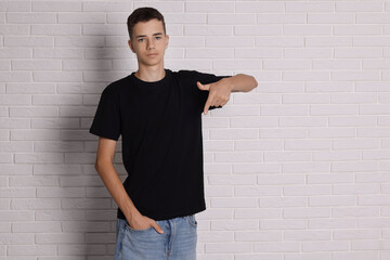 Wall Mural - Teenage boy wearing black t-shirt near white brick wall, space for text