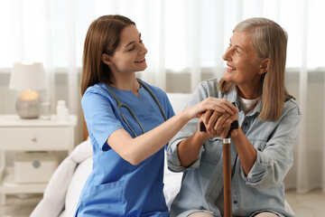 Canvas Print - Smiling healthcare worker supporting senior patient on bed indoors