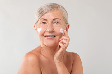 Sticker - Senior woman applying face cream on light background