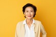 © Markus Schröder - Portrait of a glad asian woman in her 60s wearing a classic white shirt in pastel yellow background