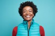 © Markus Schröder - Portrait of a joyful afro-american woman in her 40s dressed in a thermal insulation vest while standing against pastel teal background