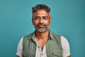 Portrait of a glad indian man in his 40s wearing a rugged jean vest in pastel teal background