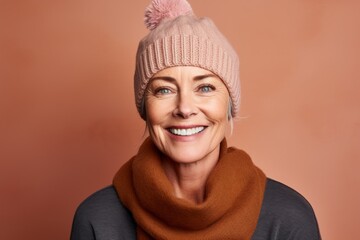 Poster - Portrait of a grinning woman in her 50s donning a warm wool beanie while standing against pastel brown background