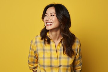 Sticker - Portrait of a grinning asian woman in her 40s dressed in a relaxed flannel shirt while standing against soft yellow background