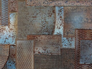 a patchwork of various rectangular and square panels with a textured, weathered appearance. The panels have a mix of rusty brown, blue, and gray tones, giving them an aged and industrial look. 