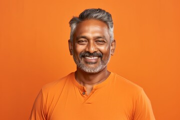 Portrait of a glad indian man in his 50s dressed in a casual t-shirt while standing against soft orange background