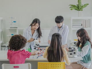 Child kid girl and boy asian young student team group learning biology and smile have fun happy with science lab technology with in the classroom has a tubetest Microscope chemicals on table