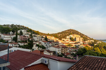 Scenic coastal village at sunset with red-roofed houses, green hills, and tranquil sea view.