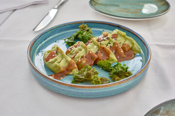 Green vegetable gyozas or dumplings with a savory sauce strawberry kimchi and crispy kale on a blue ceramic plate on a white tablecloth in a restaurant