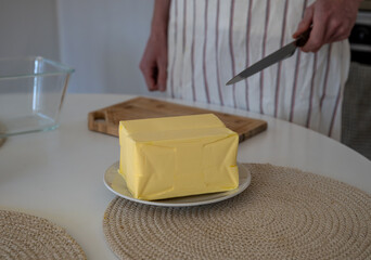 human hand cutting butter on a wooden board in the kitchen at home