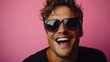 © Рудой Максим - Young man smiling joyfully against a bright pink background wearing stylish sunglasses and a black shirt