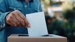 © Pinklife - A person casts a ballot into a box outdoors, capturing the spirit of civic engagement and participation in voting processes, amidst a natural backdrop.