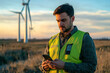 © Hunman - Portrait of a serious man engineer in a green vest shirt with a smartphone in hand against the backdrop of a windmill.