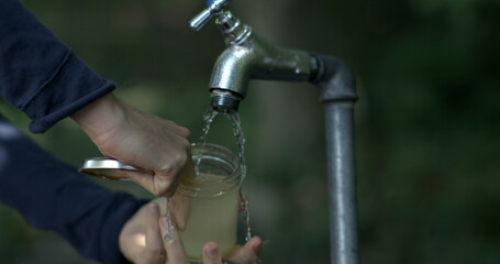 Cleaning a jar under an outdoor tap, slow-motion capture of water flow and hand interaction, emphasizing clean and refreshing hydration