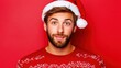 © angel_nt - A young man wearing a Santa hat and a festive sweater smiles warmly against a vibrant red background, capturing the joyful spirit of the holiday season