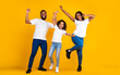 © Prostock-studio - Having Fun. Full body length of excited young black family of three dancing and fooling around. Happy African American man, woman and girl enjoying favorite music together on yellow studio background