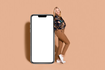 Wall Mural - Photo of blonde mature age business woman in stylish shirt folded arms stand near mobile phone touchscreen isolated on beige color background