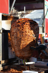 Meat al pastor on a trompo, sliced by hands with gloves for more hygiene, cooking on a rustic grill, for the preparation of traditional tacos in a street food market