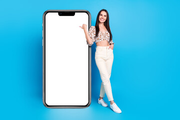 Poster - Full size photo of pretty young woman point finger empty space screen wear top isolated on blue color background