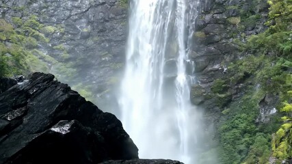 Poster - Beautiful waterfall is flowing down a rocky mountain covered by lush vegetation, creating a mesmerizing natural spectacle