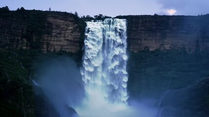 Poster - Water cascading down a steep cliff, creating a powerful waterfall with misty haze, surrounded by rocks and mountains. Twilight brings an enchanting mist and spray to this outdoor destination