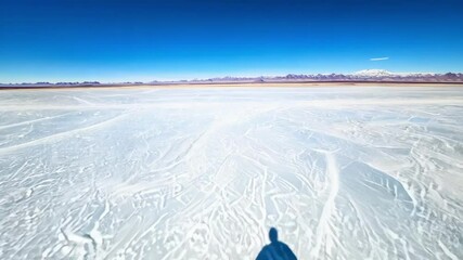 Poster - Photographer is casting a shadow on the vast salt flats, creating a striking contrast against the white surface with mountains in the distance