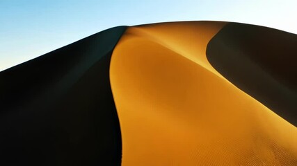 Poster - Golden sunlight illuminating a sand dune, revealing wind sculpted texture blending with the blue sky in a remote desert landscape