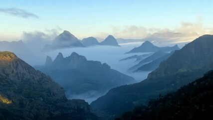 Aufkleber - Silhouettes of mountain peaks emerging from a thick fog bank during blue hour, creating a moody and atmospheric landscape