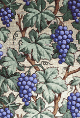  vintage wallpaper with a pattern of purple grapes and green grapevine leaves on a cream background.