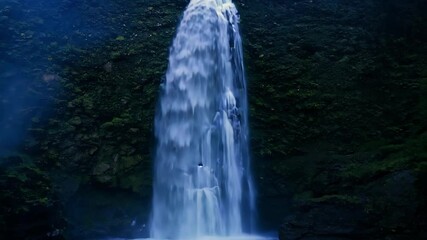 Poster - Water plunges down a mossy cliff face, creating a powerful display of nature's beauty and strength. The lush greenery surrounding the waterfall adds to the serene and tranquil atmosphere