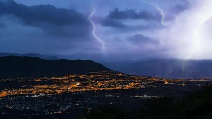 Poster - City glows at night under a twilight sky with hills and clouds, creating a serene urban landscape in , 