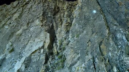Poster - Steep cliff face is illuminated by a bright light, showing the rough texture of the rock formations and the starry sky above