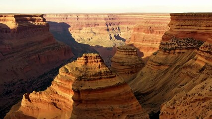 Poster - Warm sunlight is illuminating the colorful layers of rock formations creating a beautiful scene in this vast desert canyon