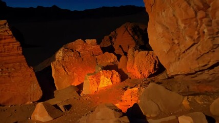 Aufkleber - Crackling fire glows between rugged rocks in the desert at night. Illuminating the dramatic landscape under the dark sky with red and orange hues. Creating a captivating display of nature's beauty