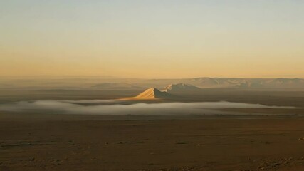 Aufkleber - The sun is rising over a desert landscape, casting a warm glow over the sand dunes and mountains in the distance as fog is slowly dissolving