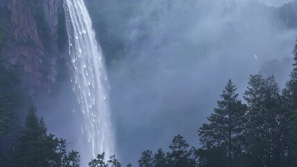 Aufkleber - Powerful waterfall is cascading down a mountainside surrounded by mist and evergreen trees, creating a beautiful and serene scene