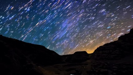 Poster - Long exposure captures the movement of the stars in the night sky, creating streaks of light that appear to be raining down over a desert canyon