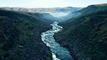 Poster - Breathtaking aerial view of a river flowing through a rugged mountain valley, with low clouds adding an ethereal touch to the landscape