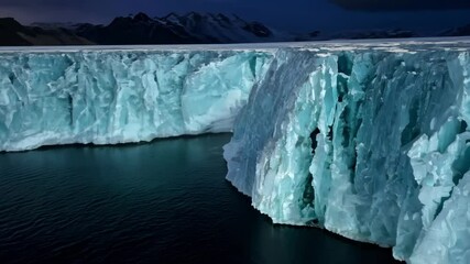 Aufkleber - Turquoise blue glacier ice is breaking off, creating an iceberg in a still, dark ocean at twilight. Mountains with snow are in the background