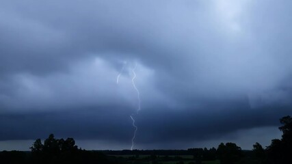Poster - Powerful lightning bolt illuminates storm clouds over a rural landscape, creating a dramatic scene in the night sky. Capturing raw forces of nature in a captivating display