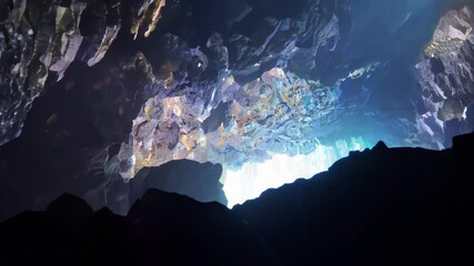 Poster - Light shines through a gap in the cave ceiling, illuminating rough rock formations, creating mysterious shadows and stunning contrast
