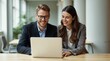 Smiling colleagues working together on a laptop during a business meeting in a modern office. They appear engaged and productive, surrounded by a bright, welcoming environment.