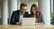 © schiers_images - Smiling colleagues working together on a laptop during a business meeting in a modern office. They appear engaged and productive, surrounded by a bright, welcoming environment.
